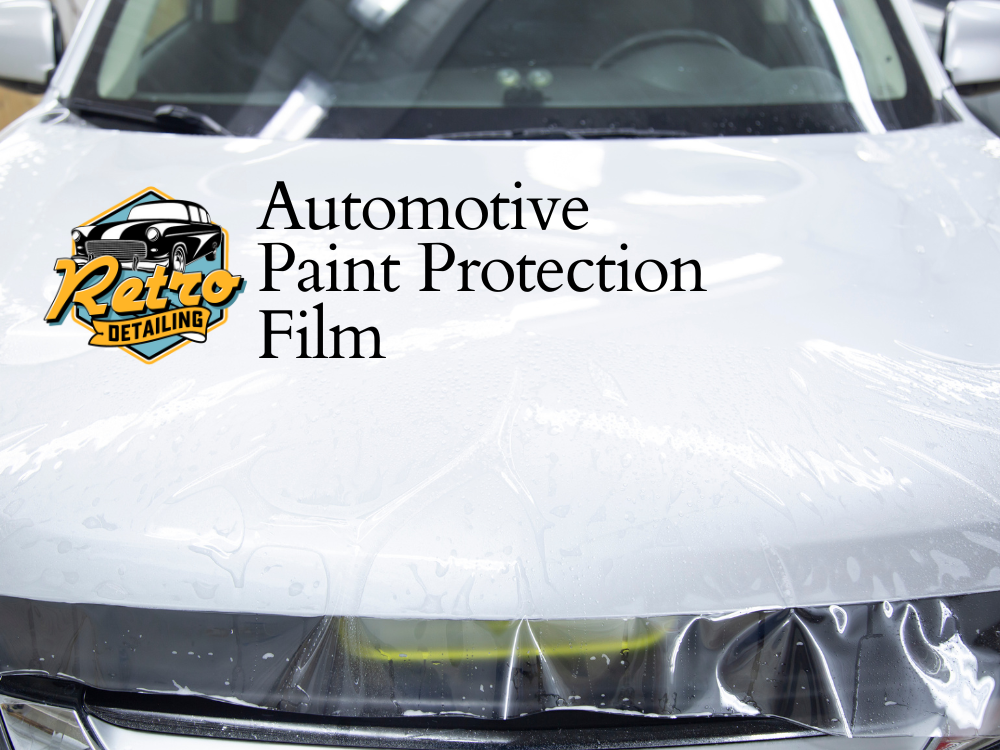 Technicians applying paint protection film to the headlight and fender of a black vehicle using squeegees and heat tools.