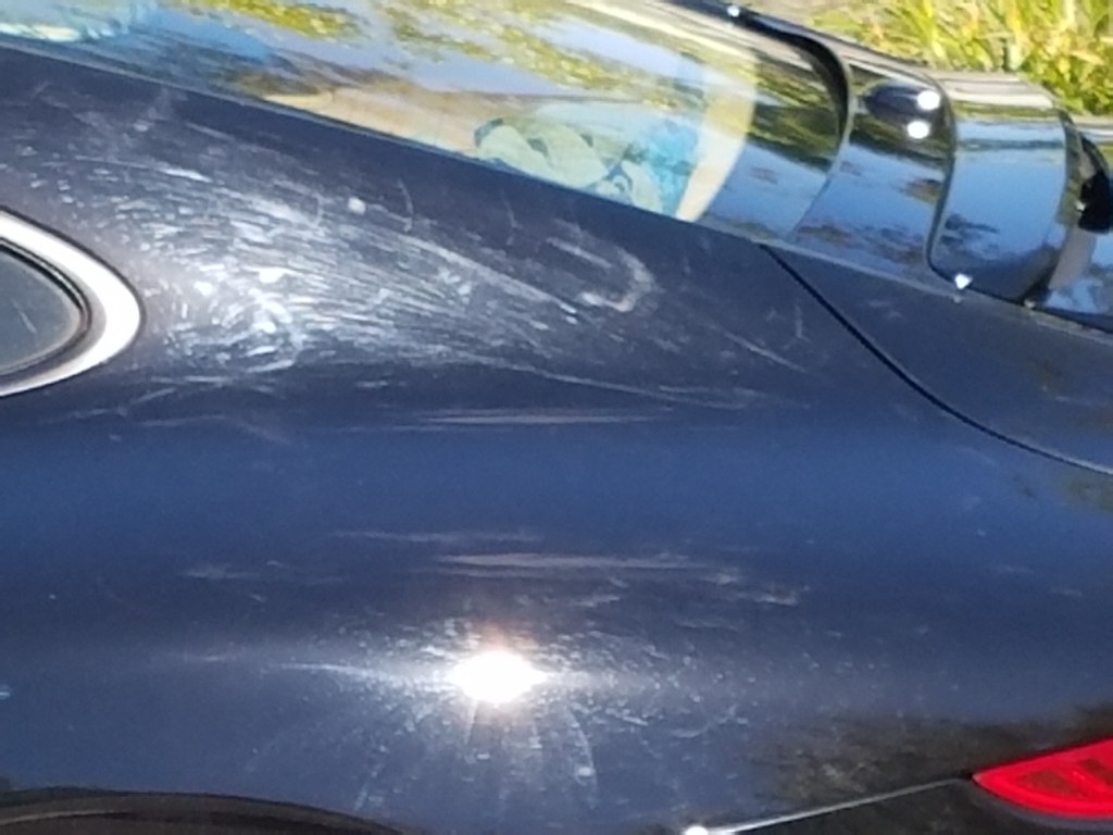 Close-up of severe buffer trails and swirl marks on a blue car's paint caused by improper polishing.